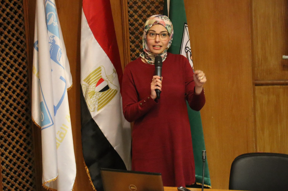 Speaker presenting beside institutional and Egyptian flags at the National Cancer Institute